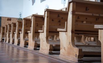 Das Bild zeigt eine mehrere Reihen an Sitzbänken aus Arvenholz in einer Kirche.