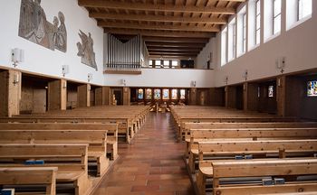 Das Bild zeigt den Innenraum einer Kirche mit vielen leeren Sitzbänken aus Arvenholz. Im Hintergrund sind grosse Orgelflöten zu sehen.